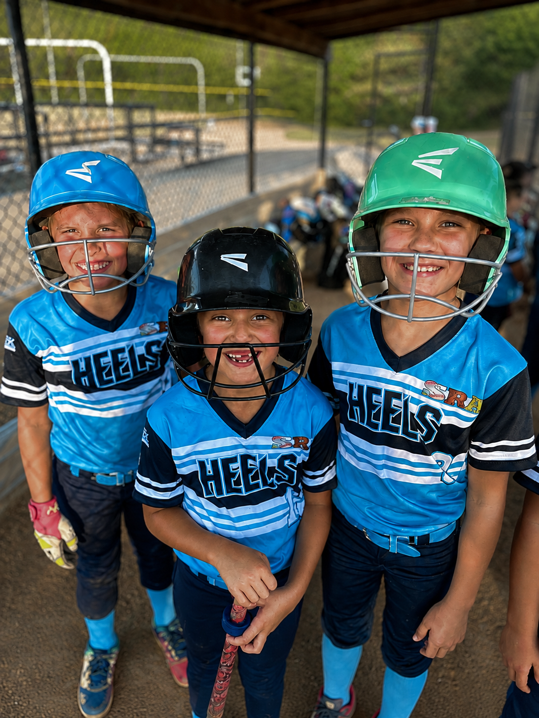 Three smiling SRA softball players in the dugout
